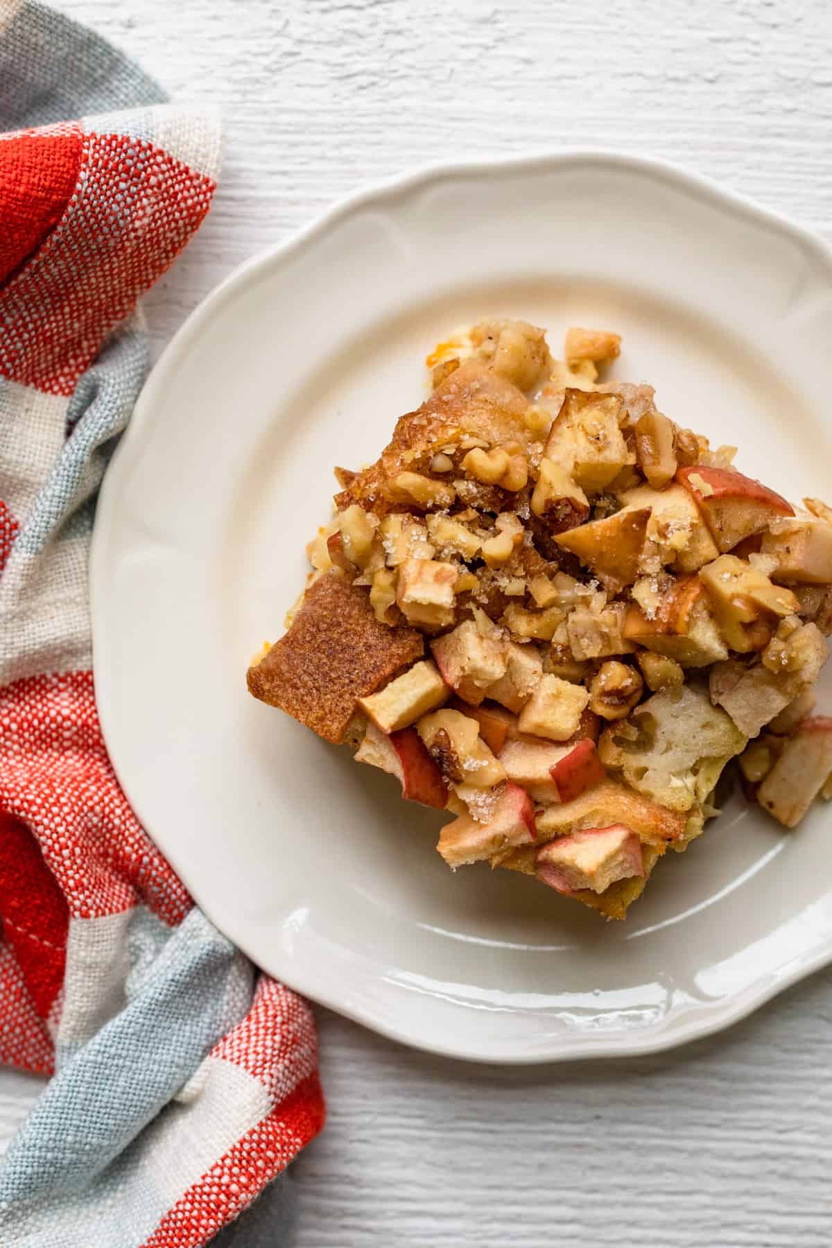 Top down view of white plate with apple bread pudding top with red kitchen towel on side