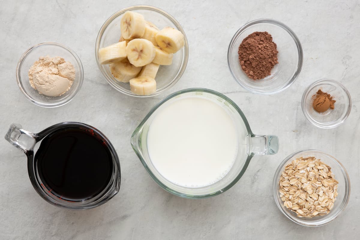 Ingredients needed to make a Breakfast Coffee Smoothie - includes cold brew coffee, milk, banana, oats, protein powder, cocoa powder, and cinnamon