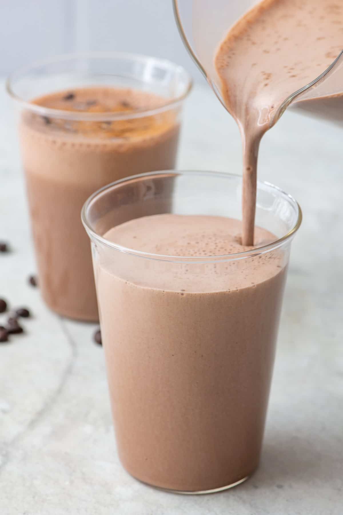 Pouring the coffee smoothie into one glass with another glass behind it.