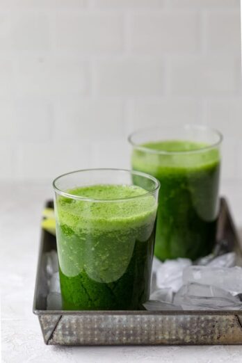 Detox kale smoothie recipe in two glass ups on a tray