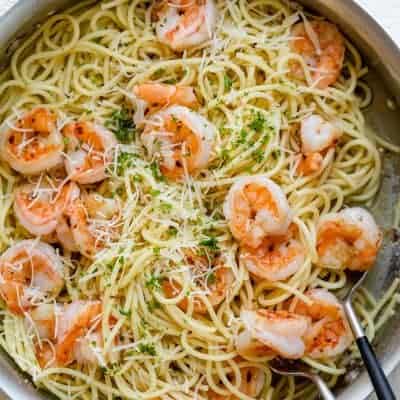 Large skillet of garlic butter shrimp pasta with serving spoon and fork in skillet
