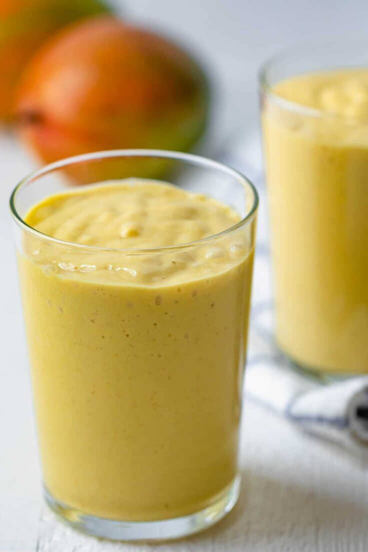 Tall glass of mango smoothie with mangos in background