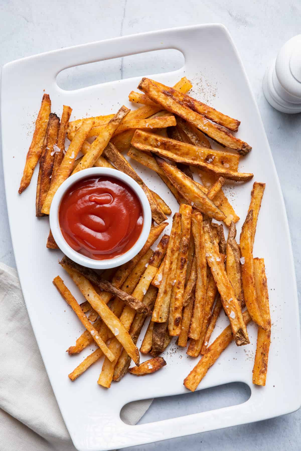 Oven baked french fries on a white plate with a small dipping bowl for the ketchup