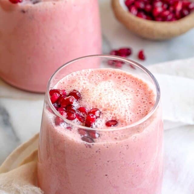 Pomegranate smoothie in glass cup with second cup in background