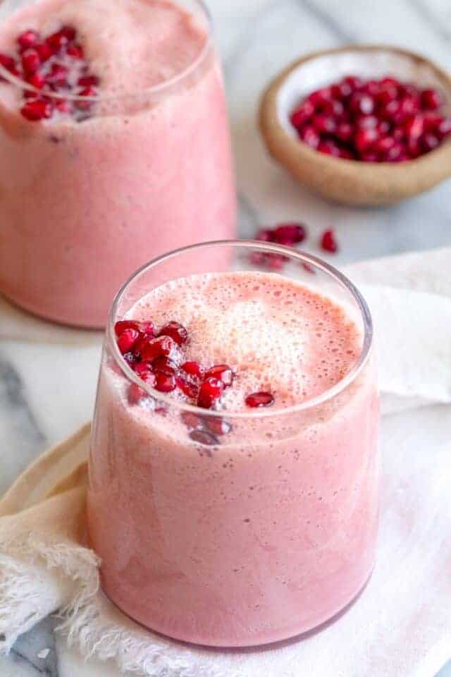Pomegranate smoothie in glass cup with second cup in background