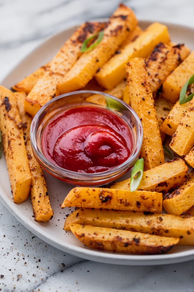 Oven baked rutabaga fries on a plate with ketchup and garnished with green onions