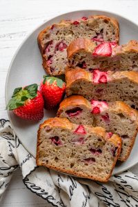 Plate of slices of strawberry banana bread with fresh strawberries on the side