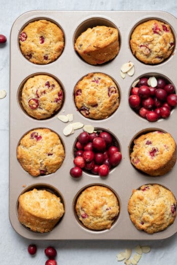 Muffin tin with baked cranberry muffins, and cranberries added in two of the muffin tins