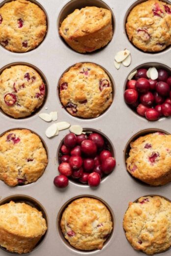 Muffin tin with baked cranberry muffins, and cranberries added in two of the muffin tins