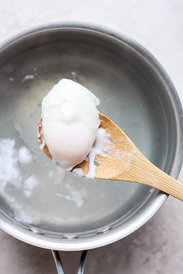 Poached egg on a wooden slotted spoon over pot with water