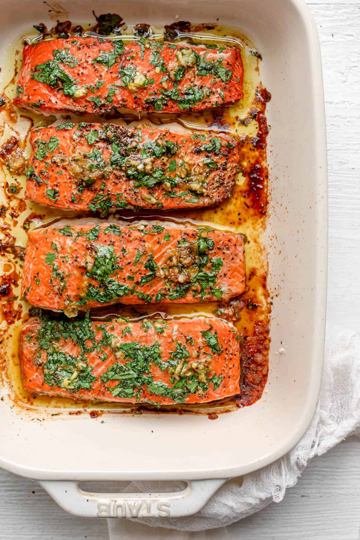 The oven cooked salmon after it's done cooking topped with garlic and cilantro in an off-white rectangle baking dish