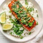 Garlic Cilantro Oven Baked Salmon in a white shallow bowl over rice with lime wedges