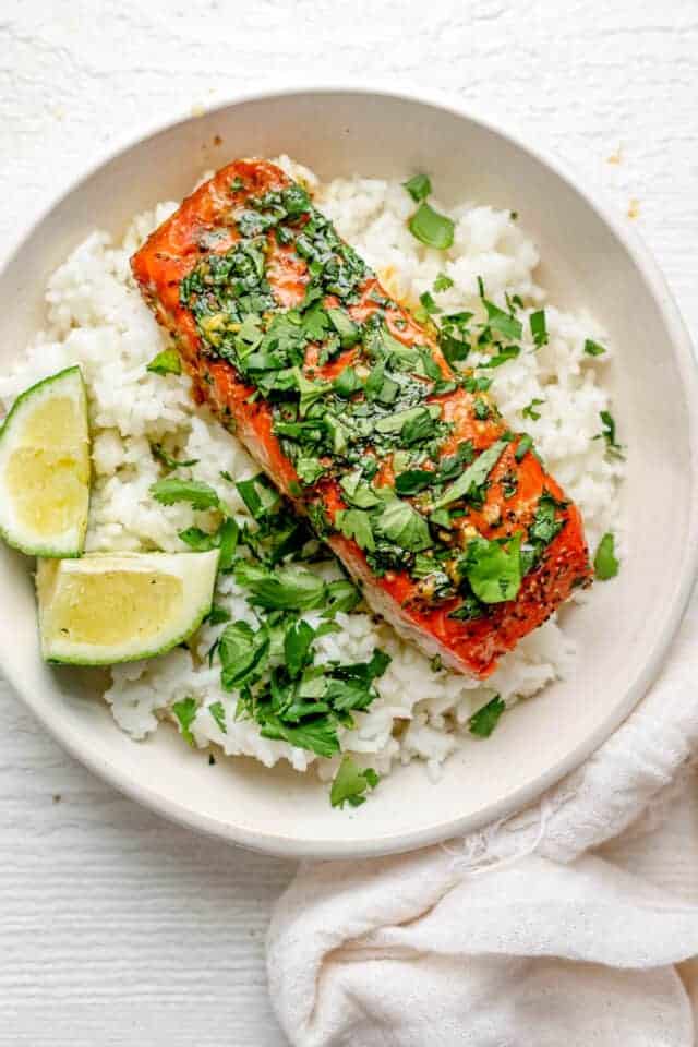 Garlic Cilantro Oven Baked Salmon in a white shallow bowl over rice with lime wedges
