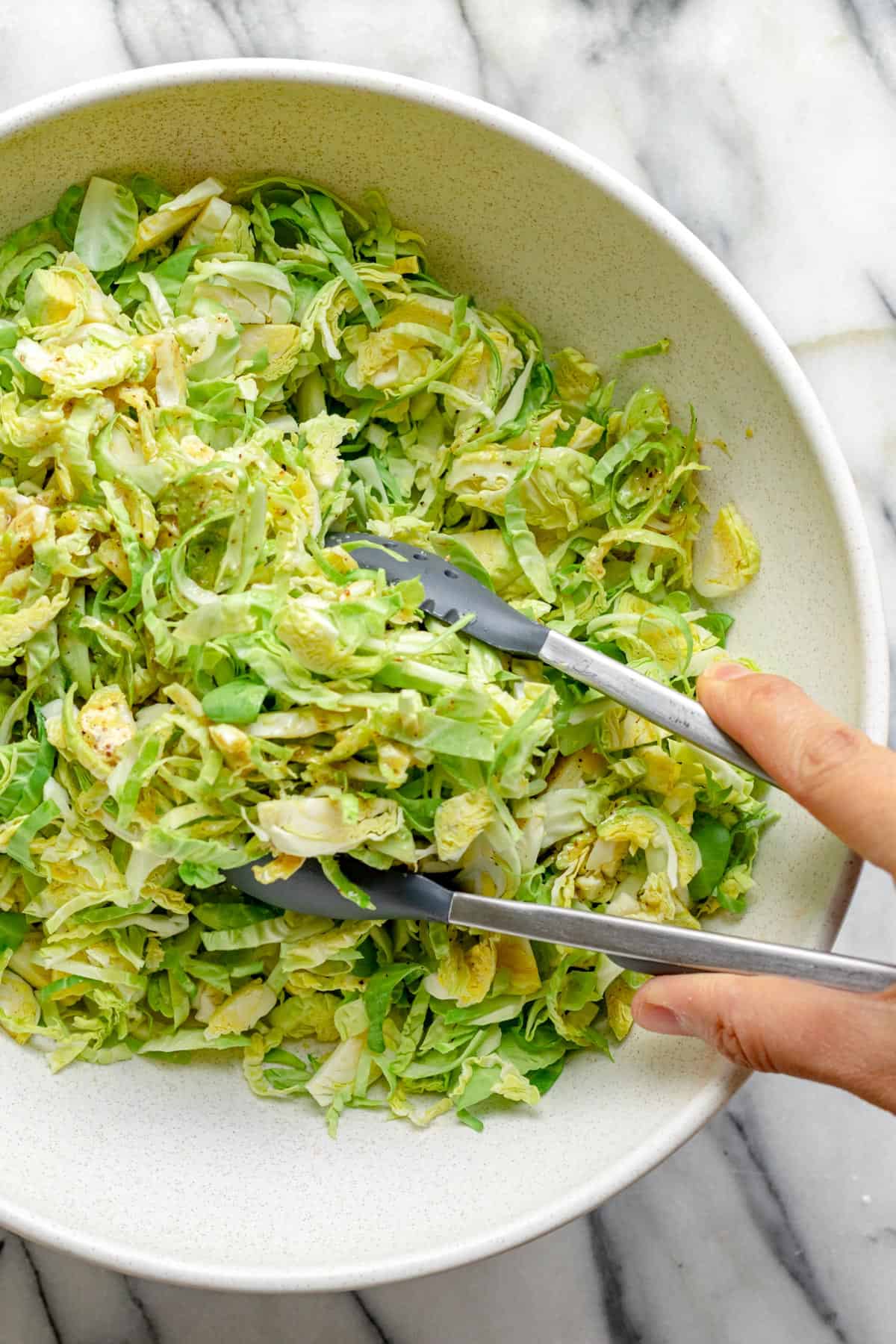 Tossing brussels with tongs in a large white bowl