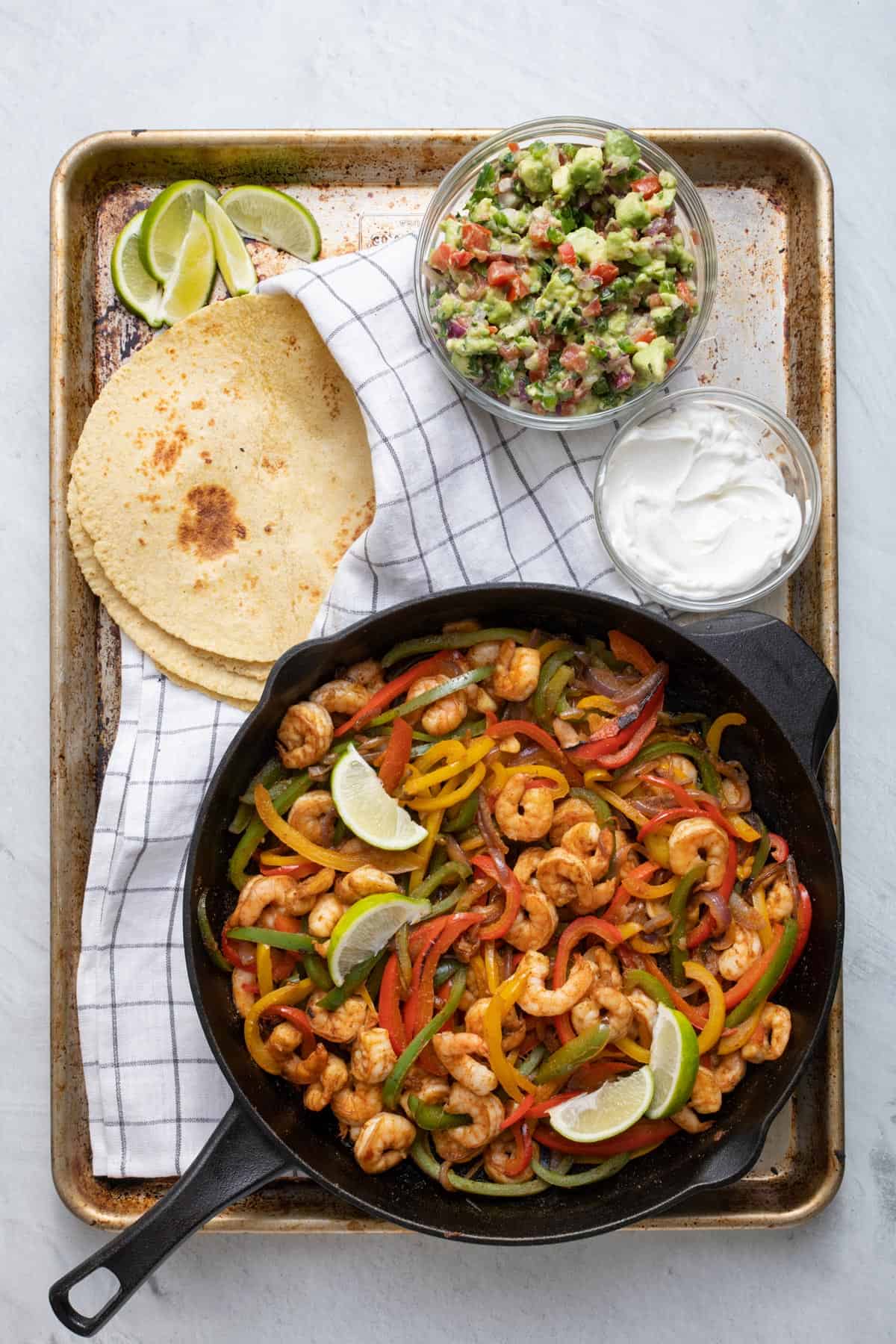 Shrimp fajitas on a tray with tortillas, sour cream and avocado salsa