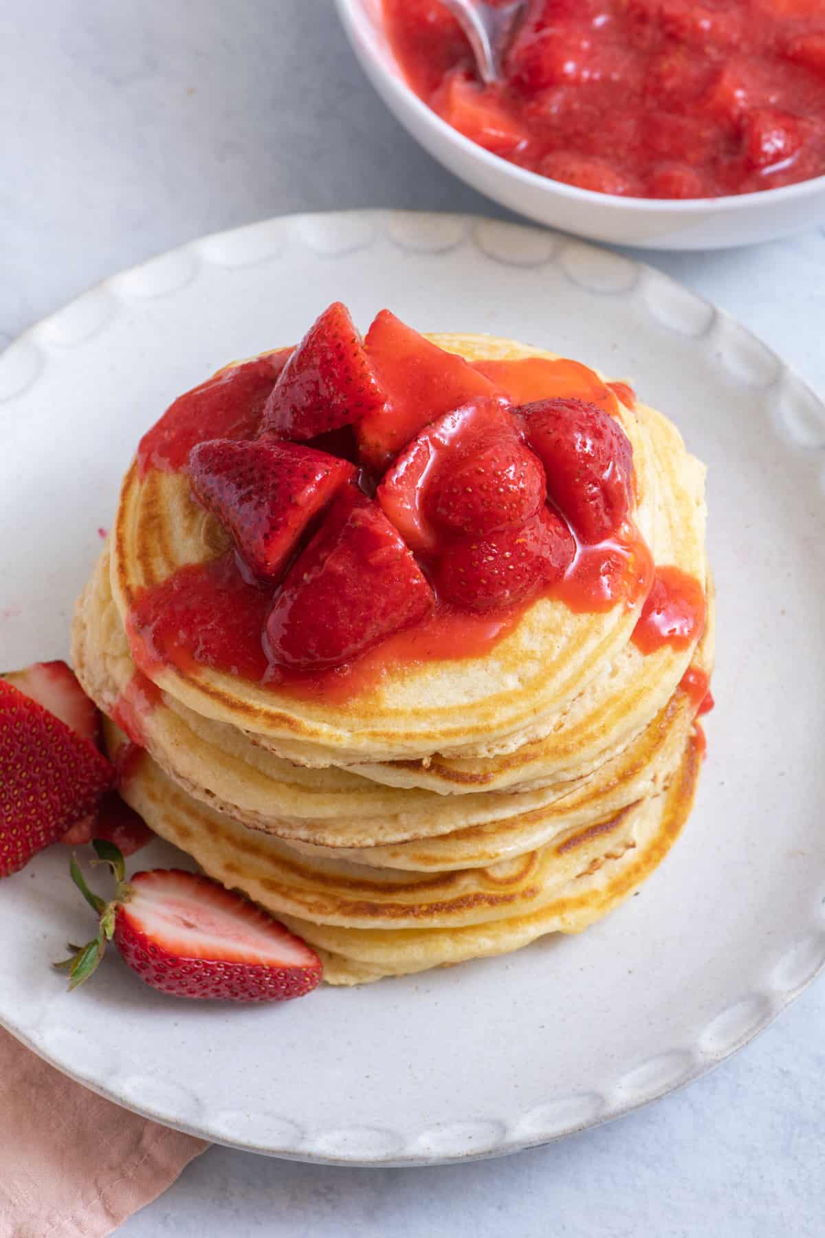 Stack of pancakes topped with strawberry sauce and garnished with fresh strawberries on a white plate.