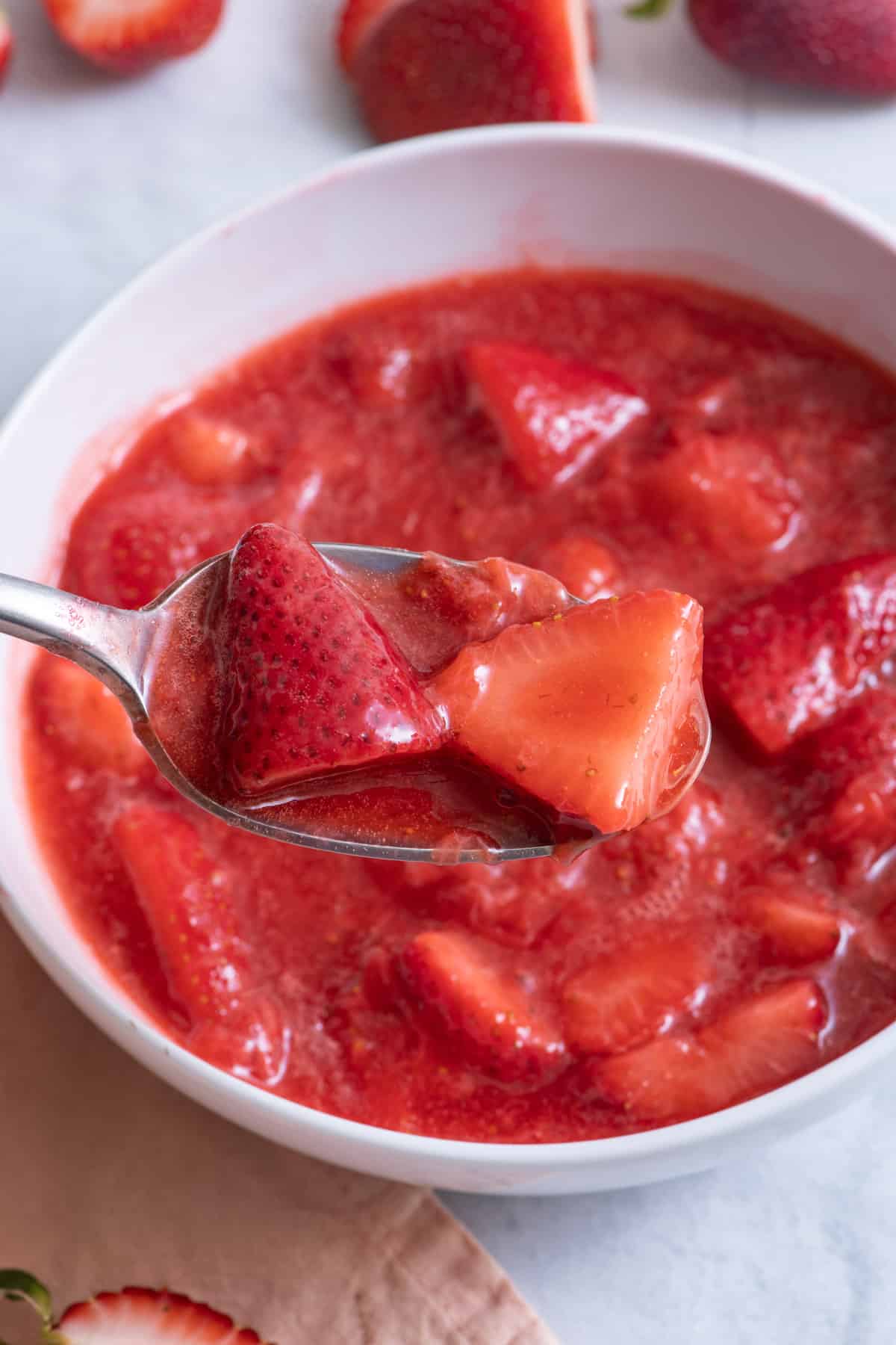 Spoon scooping out strawberries from bowl.