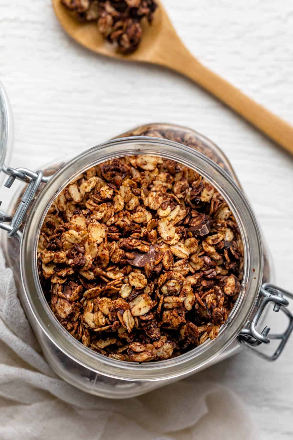 Jar canister of chocolate granola with wooden spoon on side with granola on it