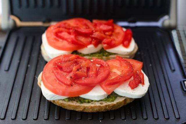 Two open faced sandwiches in the panini topped with tomatoes and roasted red peppers