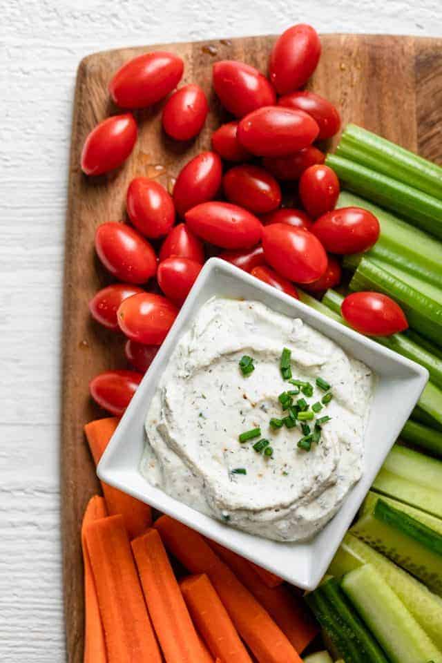 Square bowl or homemade ranch dip topped with fresh chives and surrounded by fresh vegetables