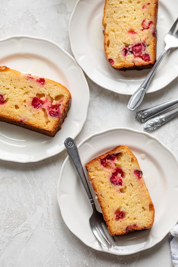 Three slices of lemon cranberry cake on small white plates with forks