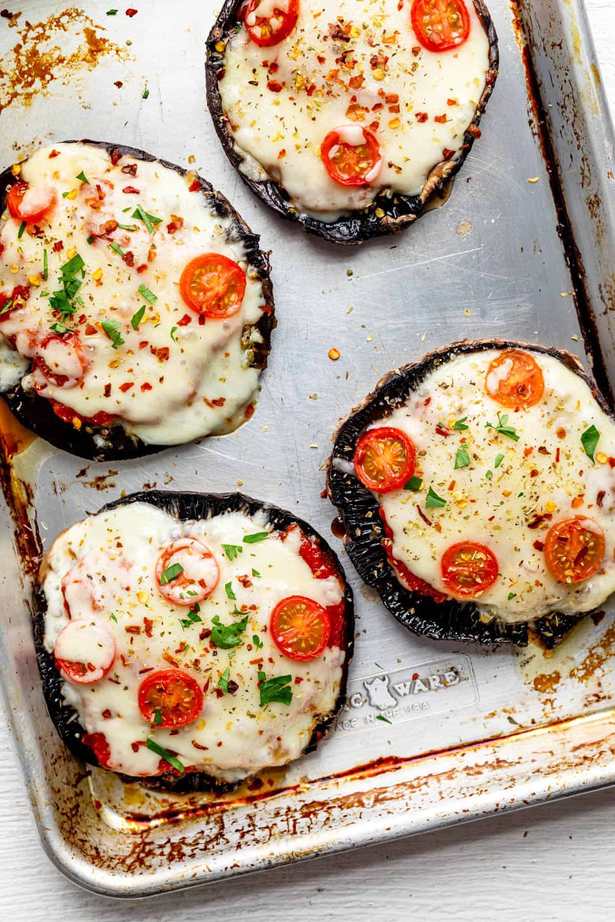 Four portobello mushrooms stuffed with pizza sauce, cheese and tomatoes on a baking dish