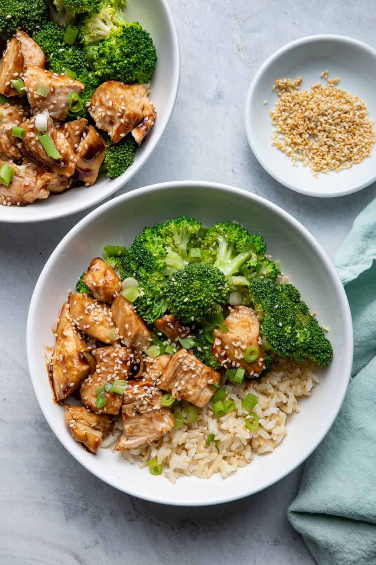 Chicken Teriyaki, Brown Rice and Broccoli in bowls with sesame seeds on the side