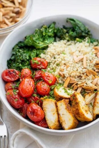 Large bowl of chicken and quinoa served with tomatoes, kale and toasted almonds