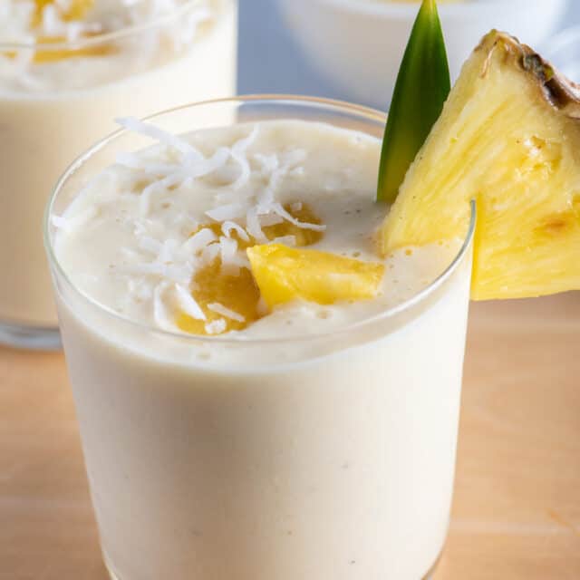 Two small cups of pina colada smoothies with pineapples on on the cup