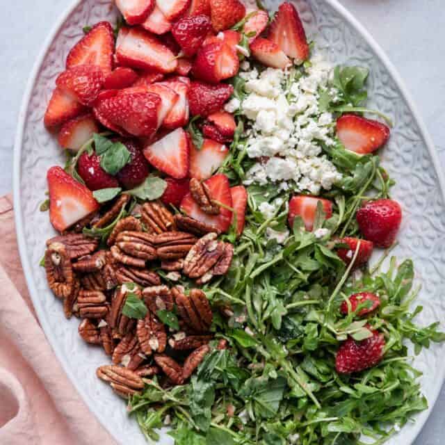 Strawberry Arugula Salad on a large platter with the dressing in a small bowl next to it