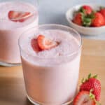 Two cups of strawberry protein smoothies topped with slices of strawberries