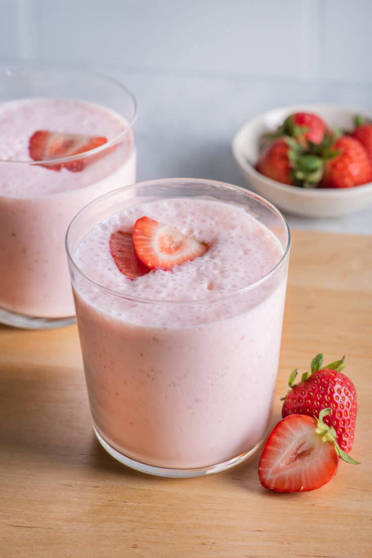 Two cups of strawberry protein smoothies topped with slices of strawberries
