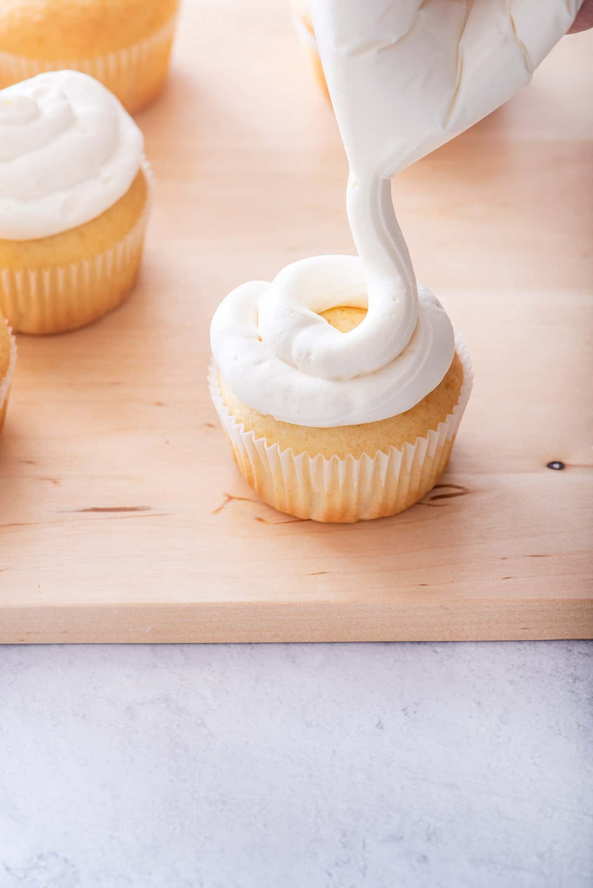 Piping cupcakes with cream cheese frosting to from ziplock bag