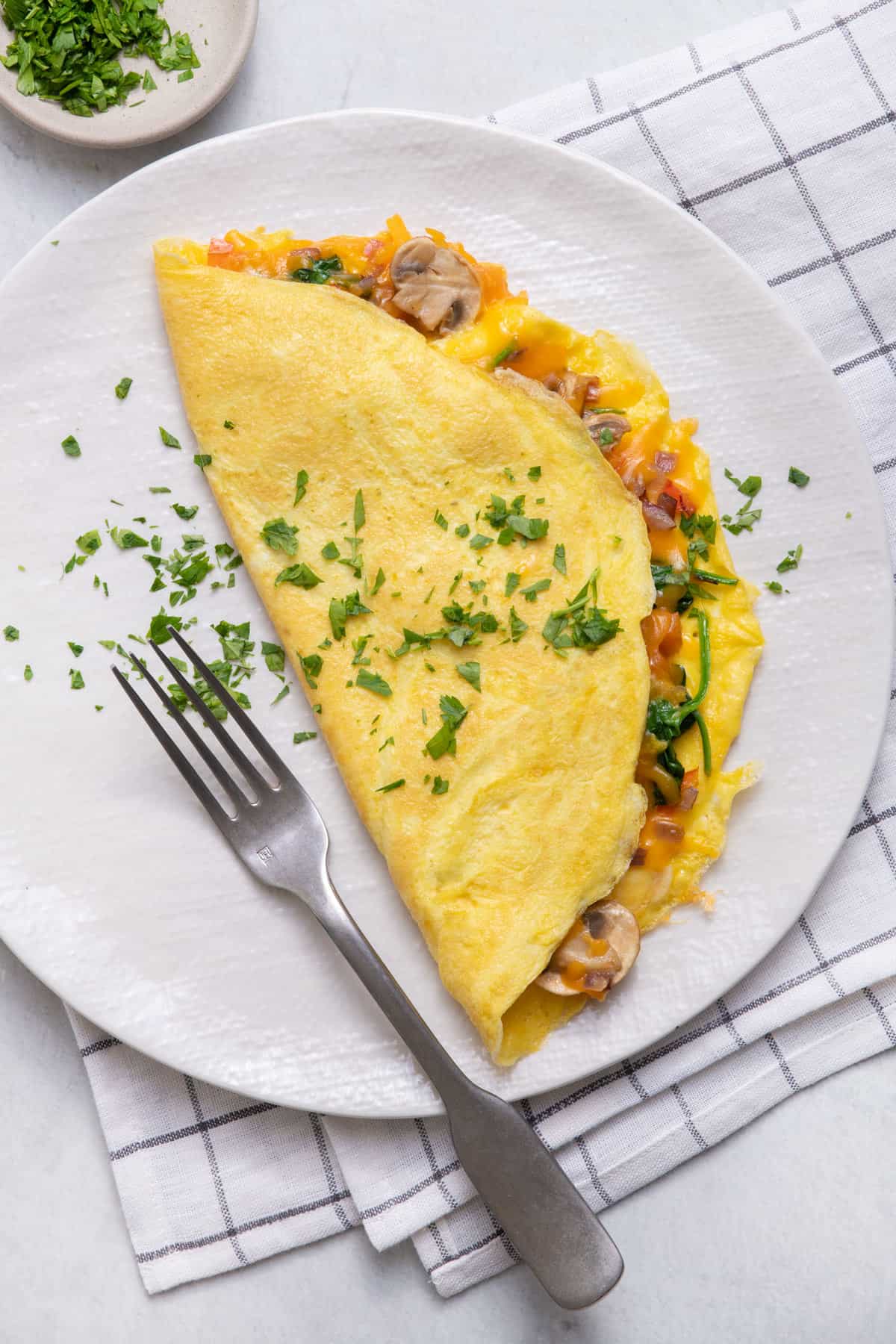 Veggie omelette garnished with parsley on white plate with fork on plate