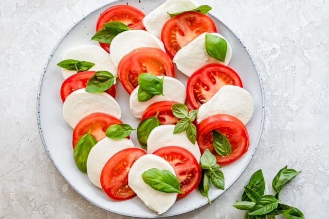 Alternating tomato and mozzarella slices with basil on serving platter