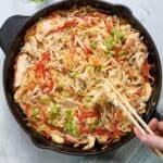Chicken and vegetables lo mein in a large cast iron skillet with chopsticks grabbing a bite