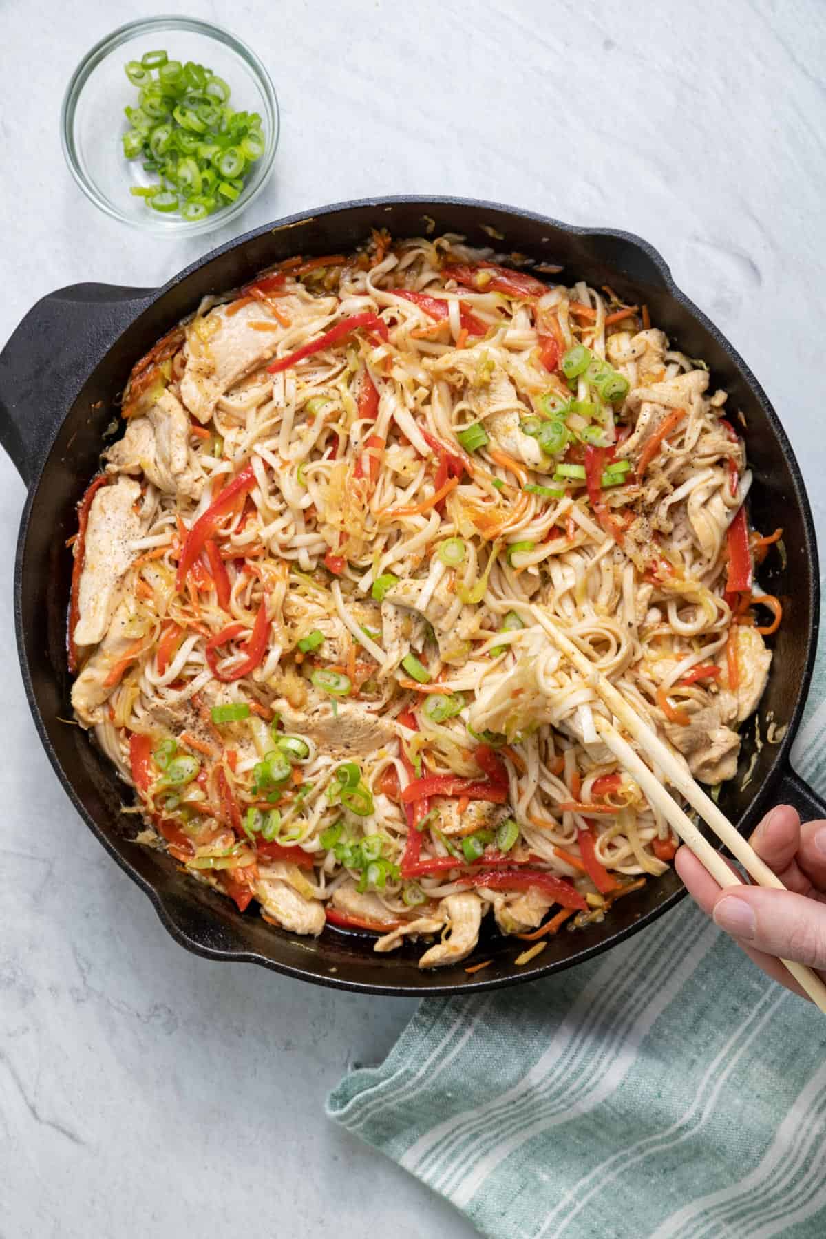 Chicken and vegetables lo mein in a large cast iron skillet with chopsticks grabbing a bite