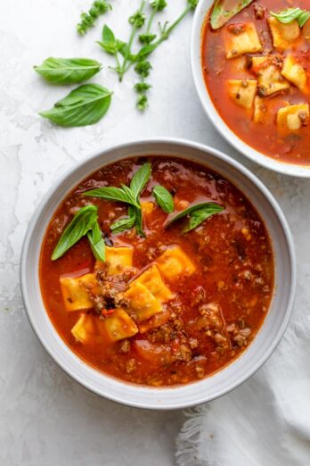 Large bowl of ravioli soup made with ground beef and garnished with basil