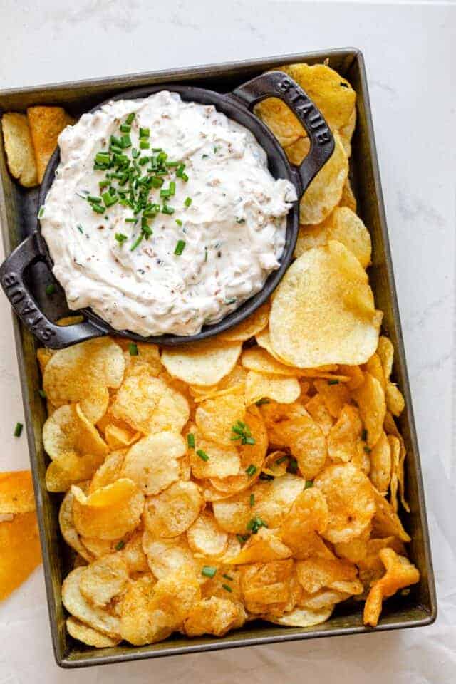 Homemade french onion dip in a small bowl with potato chips around it in small tin