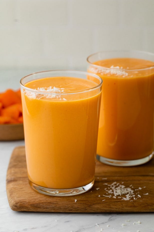 Two cups of mango papaya smoothie topped with shredded coconut