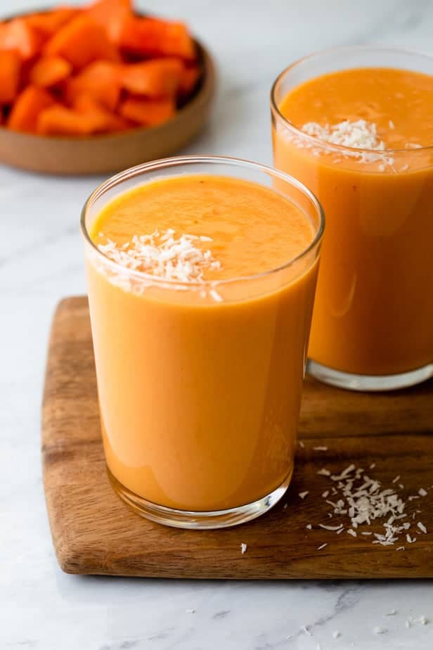 Mango papaya smoothies in clear cups with bowl of papaya in the background