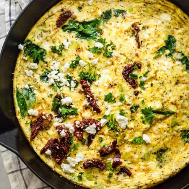 Mediterranean Frittata in a cast iron skillet topped with sundried tomatoes, feta cheese and parsley