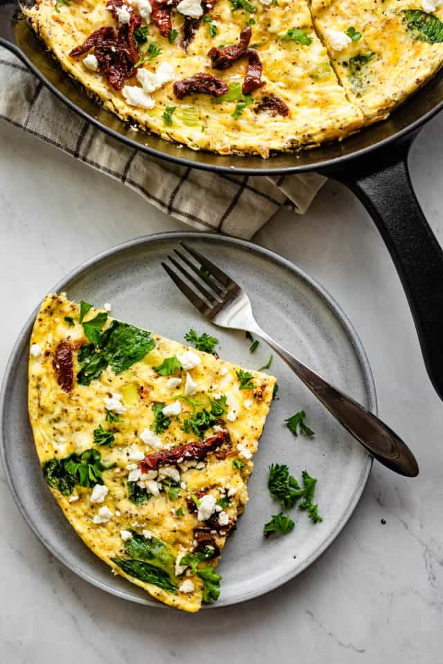 Slice of the Mediterranean frittata in a small round plate with a fork next to it.