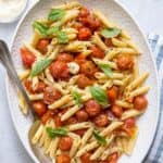 Long serving platter of roasted tomatoes tossed with penne pasta and garnished with basil.