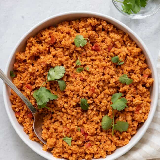 Large bowl of tomato rice with spoon inside and garnished with cilantrol