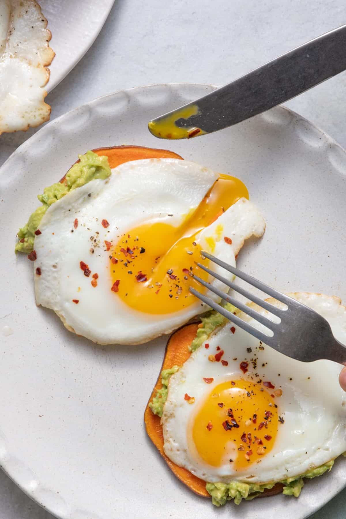 Fork and knife cutting into sweet potato toast with fried egg