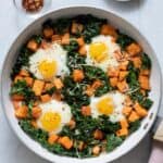 Sweet potato and kale hash with four sunny up eggs cooked in garnished with red pepper flakes and Parmesan cheese.