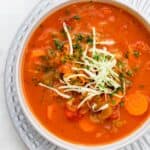 Tomato cabbage soup in a white bowl topped with fresh cabbage