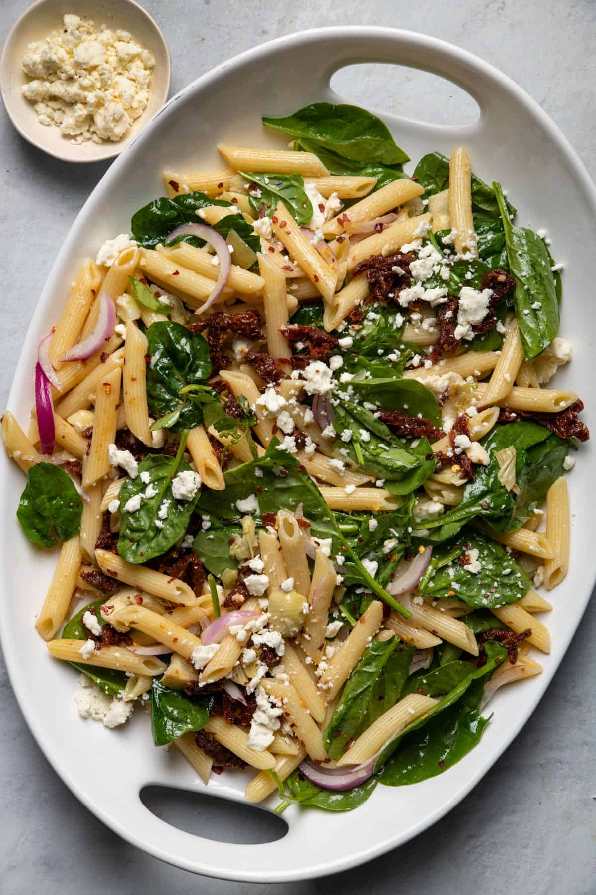 Large platter of spinach pasta salad served with sundried tomatoes and feta cheese