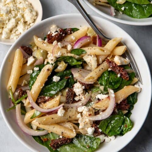 Spinach Pasta Salad in a white bowl on a table with another bowl next to it and feta cheese